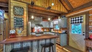 Une cuisine rustique aux murs en bois, avec un comptoir de bar en bois et un lambrequin à carreaux aux fenêtres.