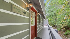 Une cabane avec une pancarte indiquant « Bienvenue à la cabane », une porte rouge et un porche doté d’un paillasson noir.