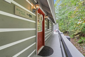A cabin with a 'Welcome to the Cabin' sign, a red door, and a porch with a black doormat.