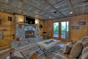 A cozy cabin interior with a stone fireplace, wooden walls, a plaid sofa, and a bench.