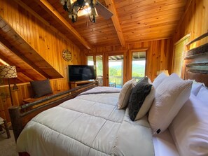 A wooden cabin bedroom with a large bed, a television, and a view of the outdoors.