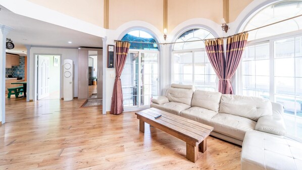 Amplia sala de estar con sofá color beige, mesa de centro de madera y ventanas grandes con cortinas.