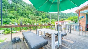 Una terraza al aire libre con una mesa y bancos, rodeada de exuberante vegetación y un paisaje de montañas.