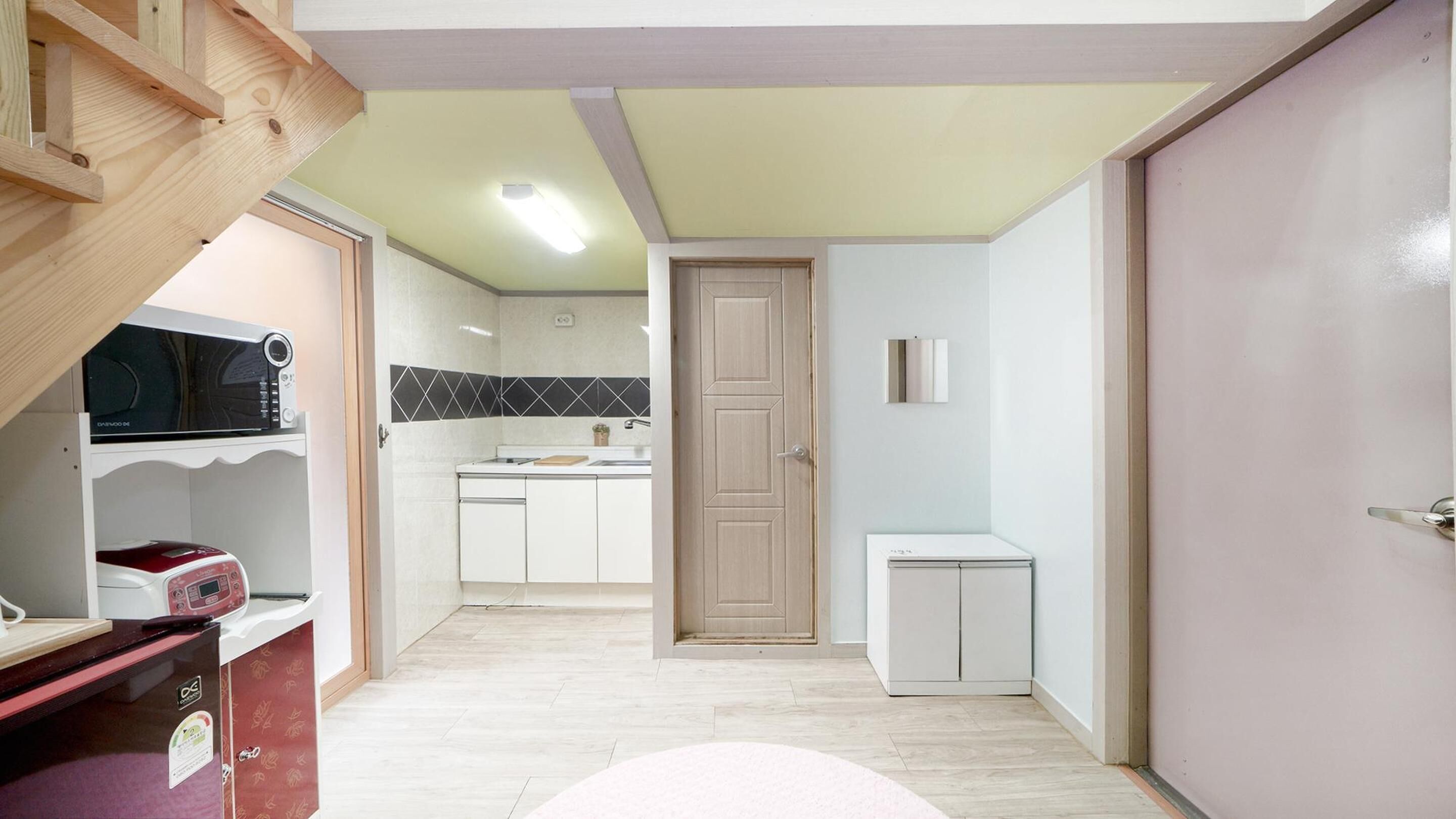 Una cocina compacta con armarios blancos, una puerta de madera y una pequeña encimera.