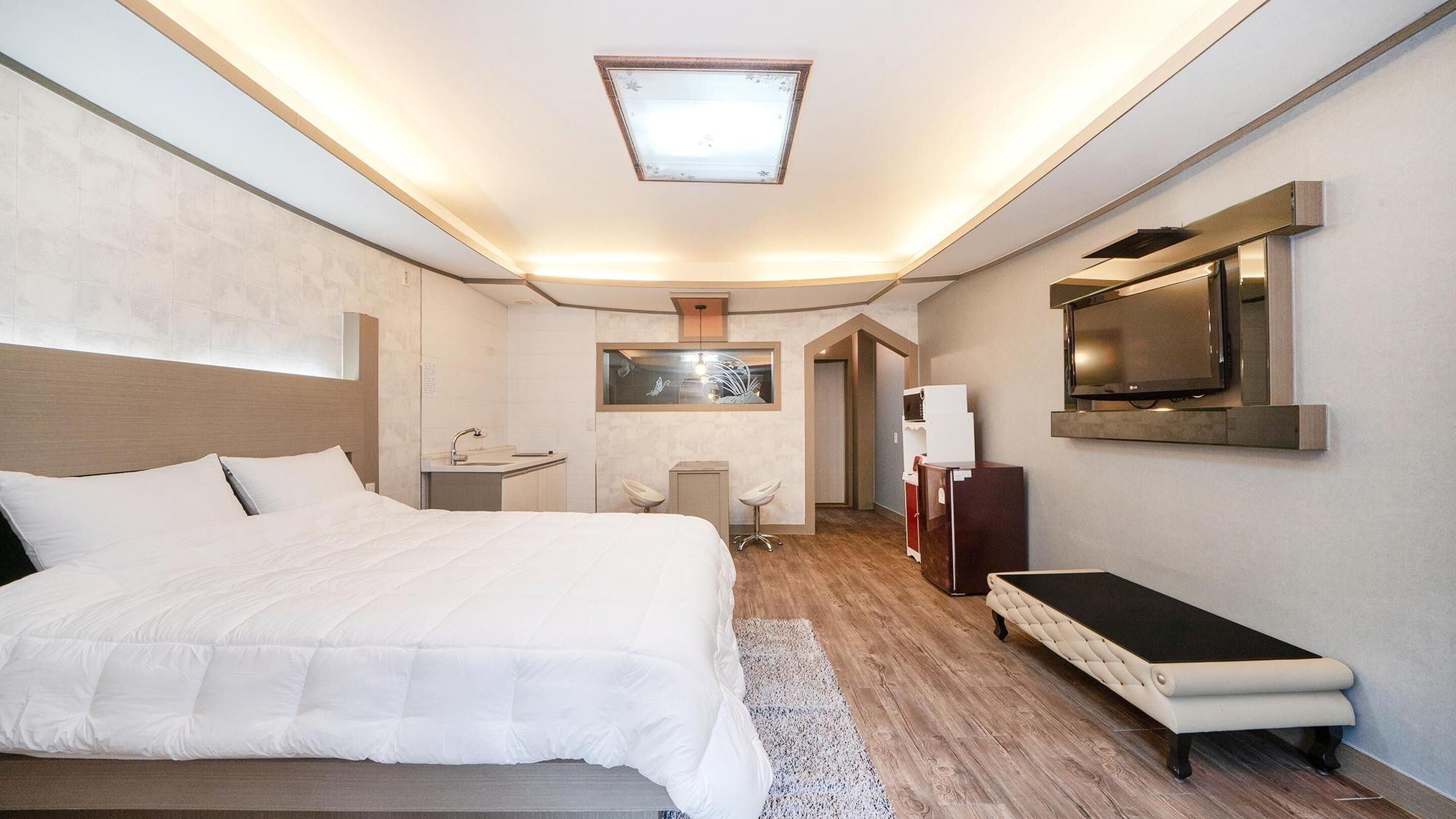 A hotel room with a bed, a desk, a TV, and a small seating area.