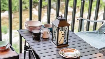 A wooden table with a lantern, bowls, and mugs on a balcony.