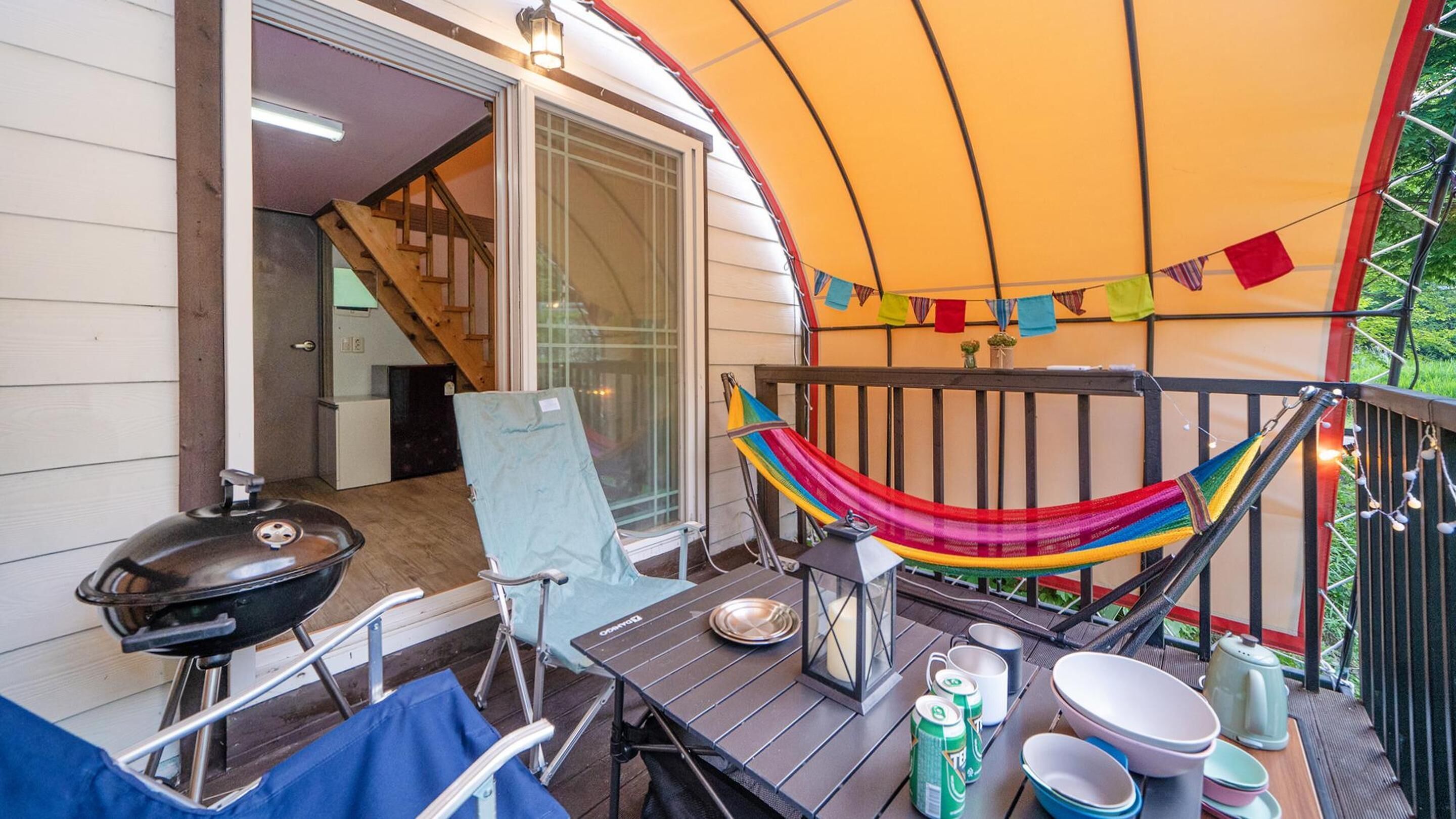 A deck with a hammock, a grill, a table with plates and cups, and a colorful flag decoration.