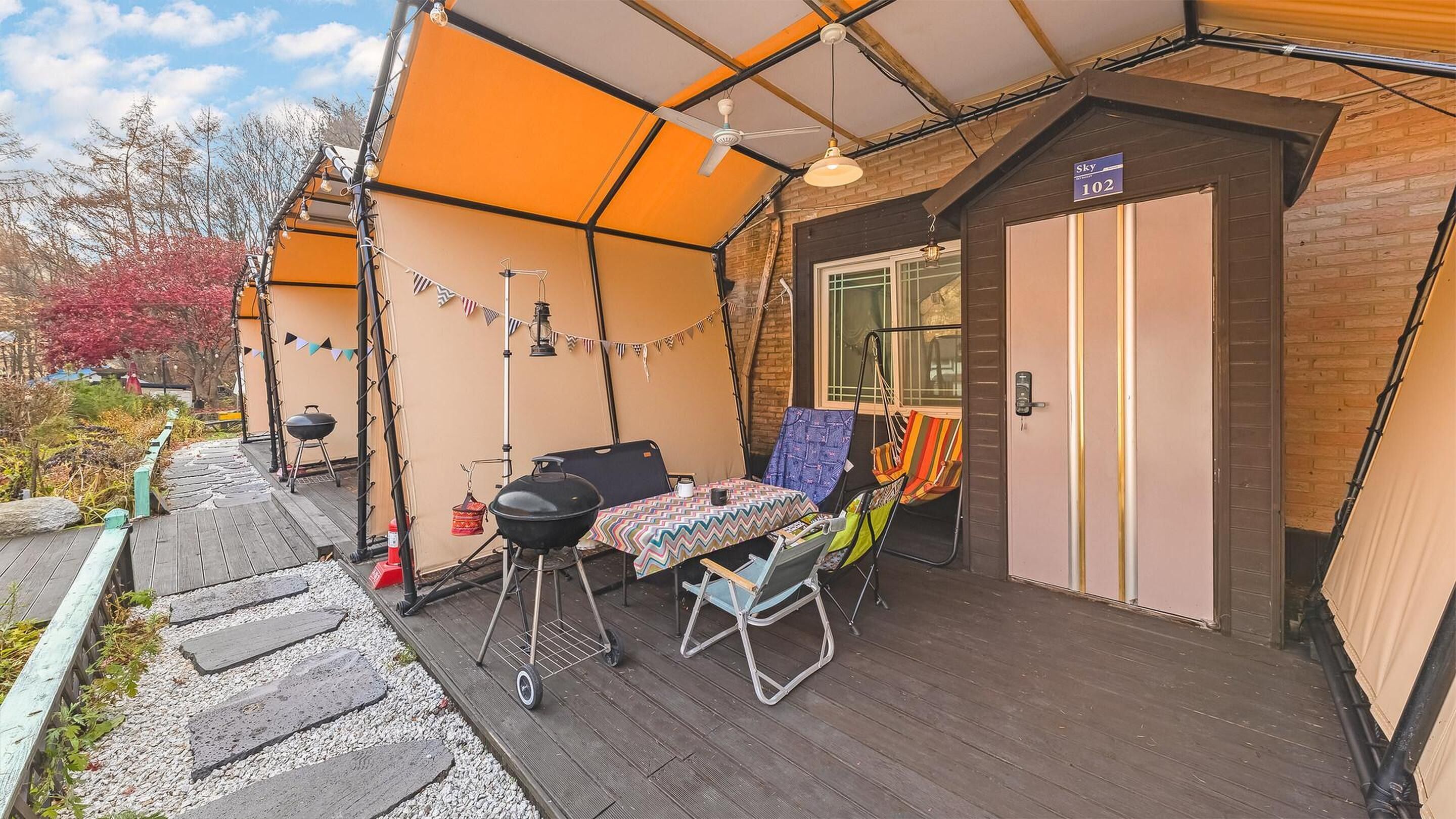 A covered outdoor area with a table and chairs, a barbecue grill, and a door labeled "Sky 102".