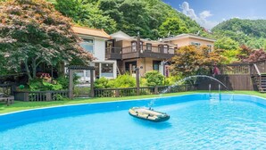 Una piscina con fuente de agua, rodeada por una terraza de madera y abundante vegetación.