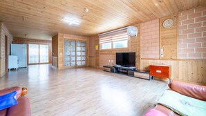 A spacious living room with wooden floors, a television, a clock, and a brick wall. - Samcheok Dasarang Pension (Samcheok)