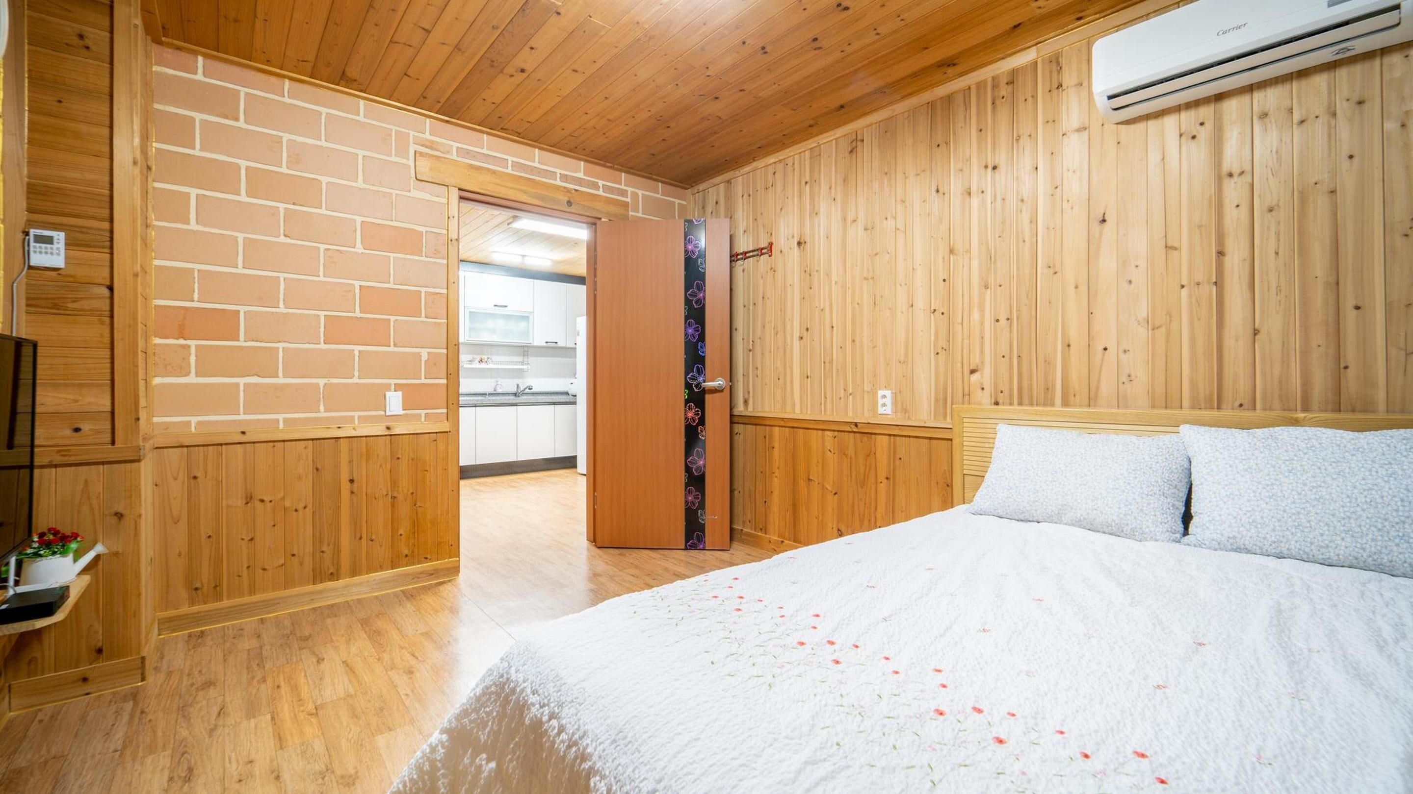 Una camera da letto con soffitto in legno, parete in mattoni, una porta in legno e un letto con copripiumino bianco.