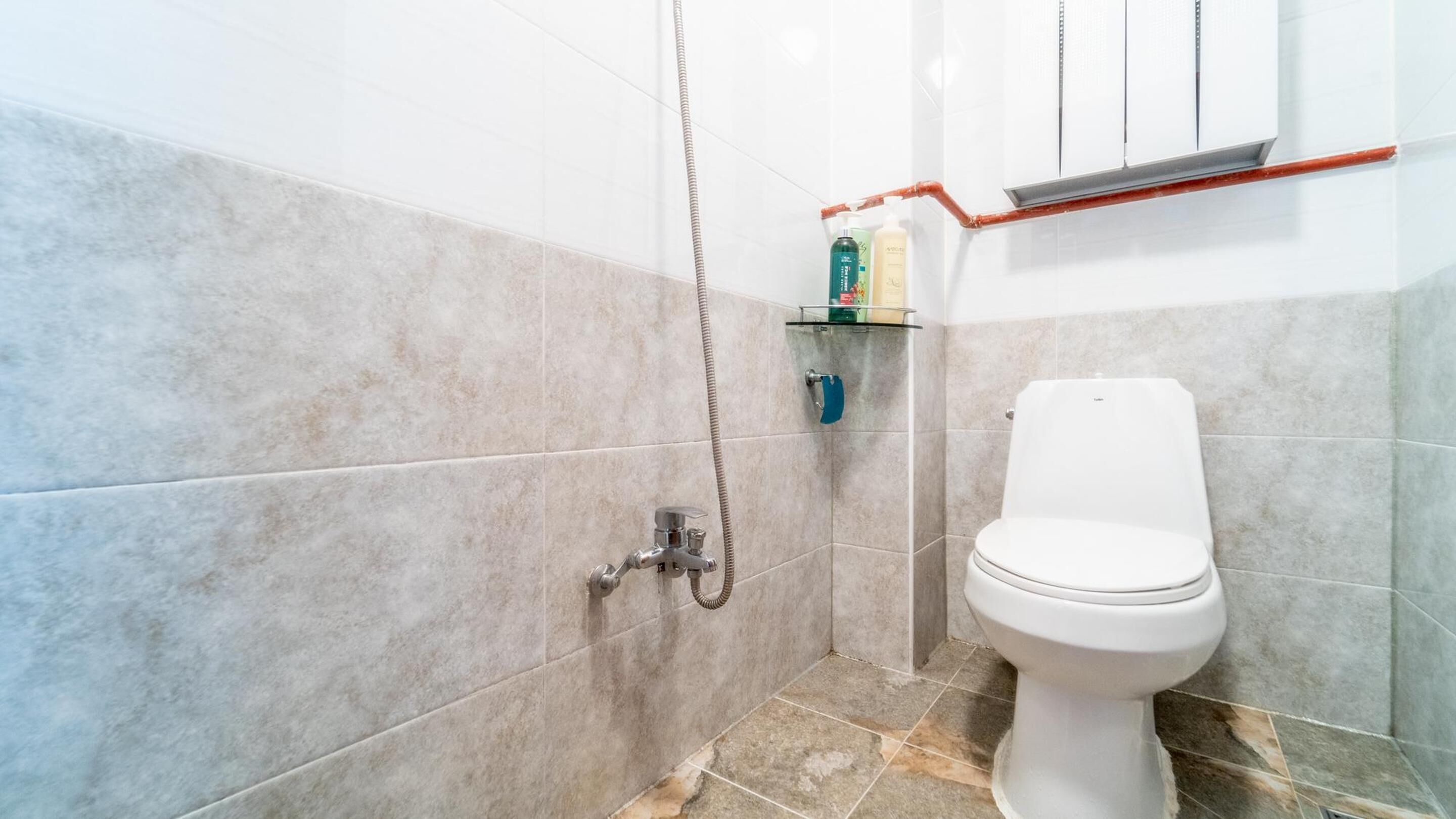 Uma casa de banho com chuveiro, sanita e um espaço para produtos de higiene pessoal.