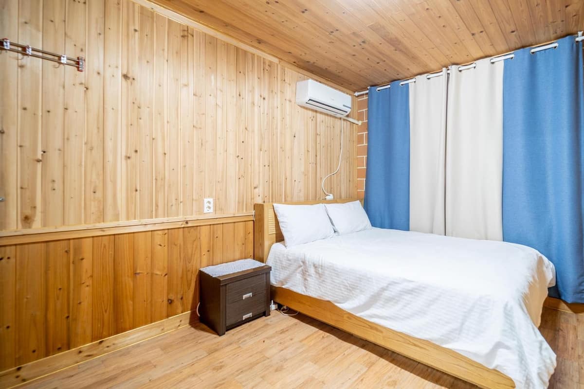 A wooden-paneled room with a bed, a small bedside table, and a wall-mounted air conditioning unit.