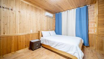 Una habitación con paneles de madera, una cama, una mesita de noche y un aire acondicionado instalado en la pared.