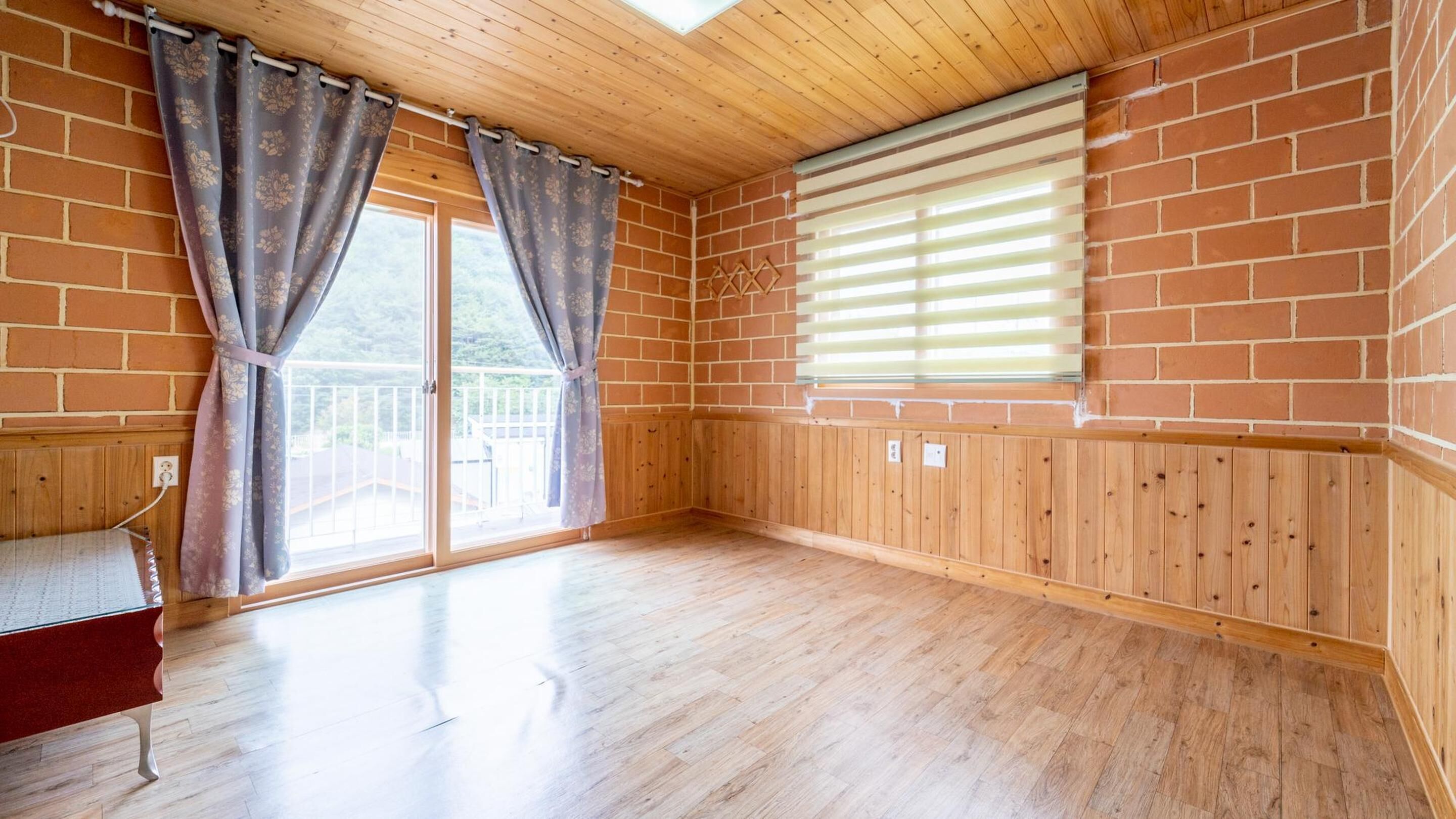 A room with wooden flooring, a sliding glass door, and a window with blinds.