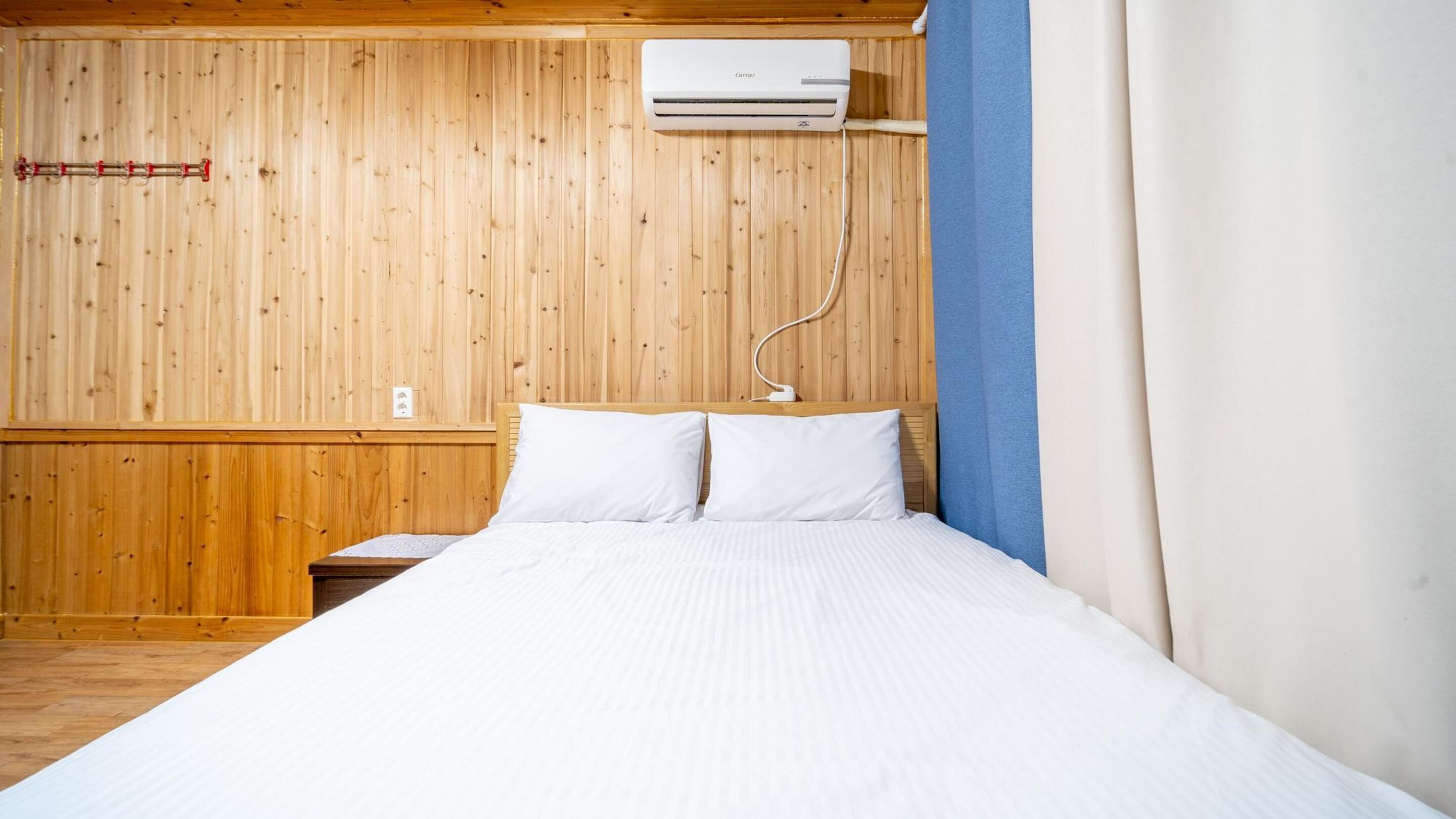 A room with a wooden paneled wall, a bed with white bedding, and a mounted air conditioner.