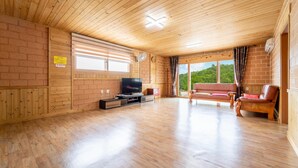 A wooden interior with a TV, sofa, and large windows overlooking greenery. - Samcheok Dasarang Pension (Samcheok)