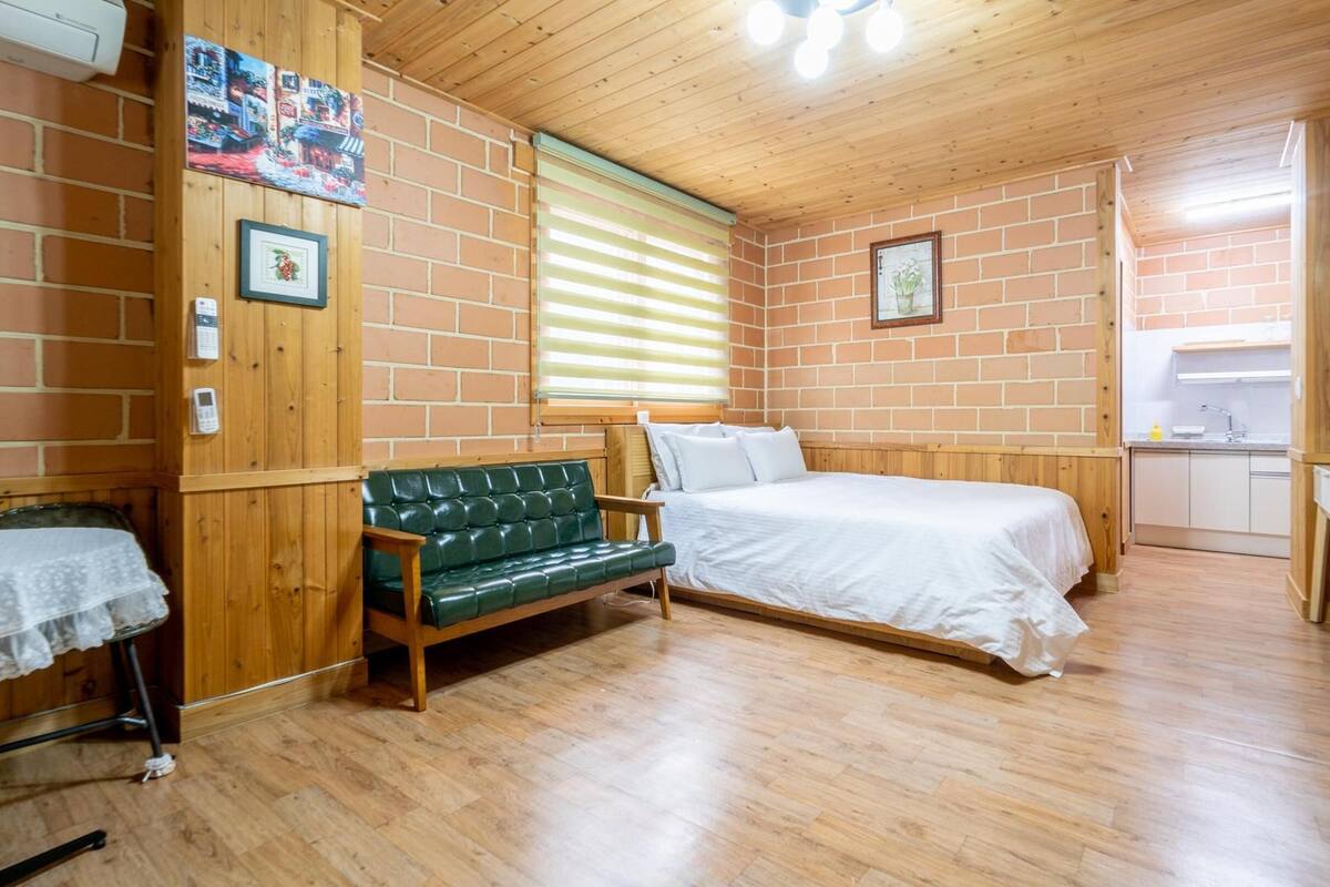 A cozy room with a wooden bench, a bed, a small desk, and a window with blinds.