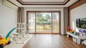 A spacious room with a large sliding glass door leading to a balcony, a play area with toys, and a white TV stand. - Jeju Sigan Yeohaeng Huyang Pension (Jeju City)
