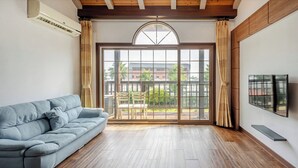 A modern living room with a sofa, a large window, and a TV mounted on the wall. - Jeju Sigan Yeohaeng Huyang Pension (Jeju City)