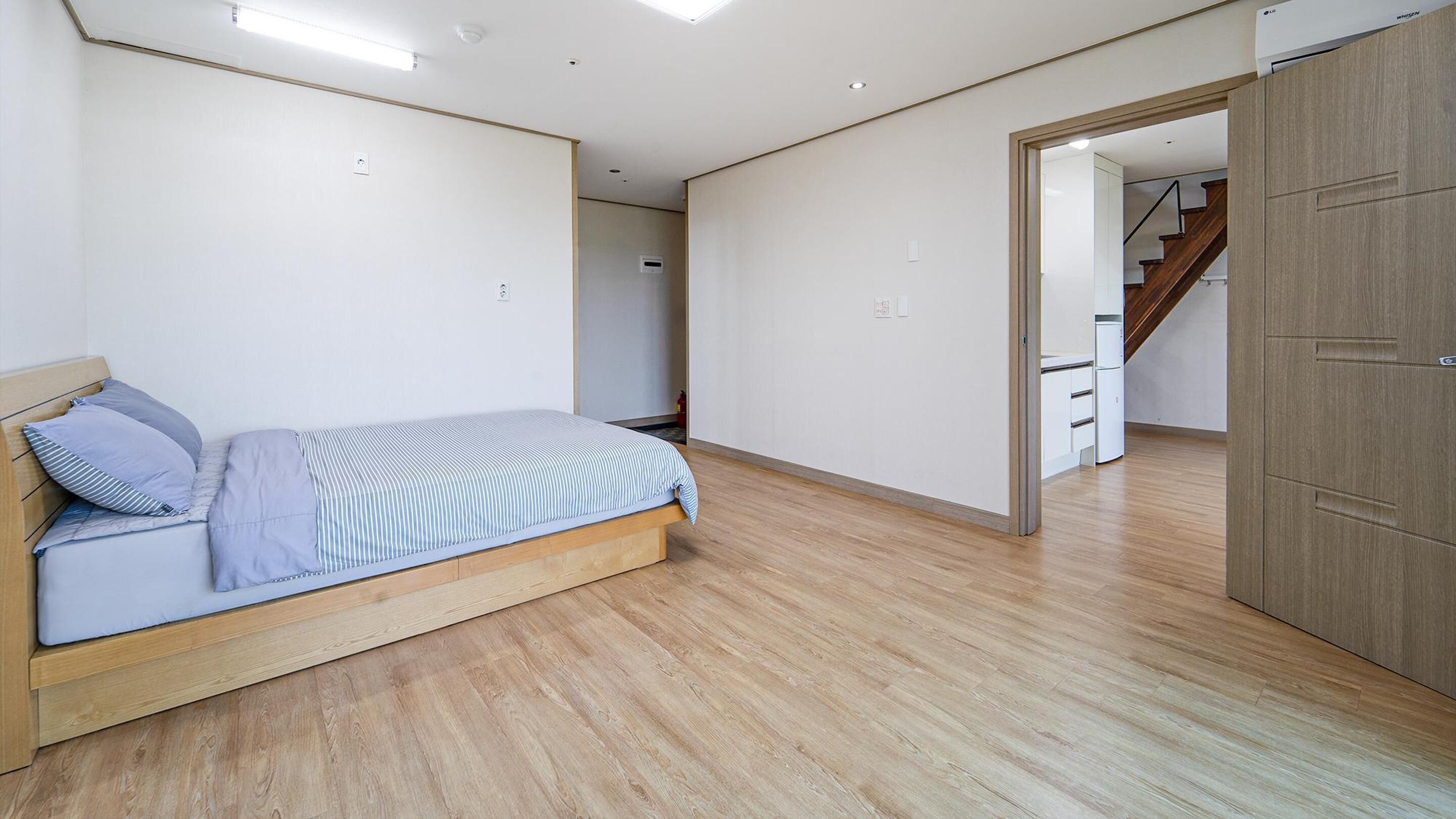 A bedroom with a bed, wooden flooring, a wardrobe, and a staircase leading to another room.