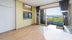 Une pièce avec un plancher en bois, une table blanche, un canapé vert, un téléviseur, un climatiseur et un balcon avec vue.