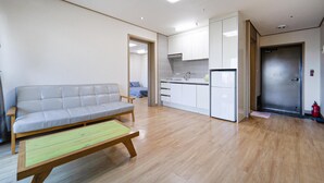 A modern living room with a grey sofa, wooden coffee table, and a kitchen area with white cabinets and a white refrigerator. - Seogwipo Narsha Resort (Seogwipo)
