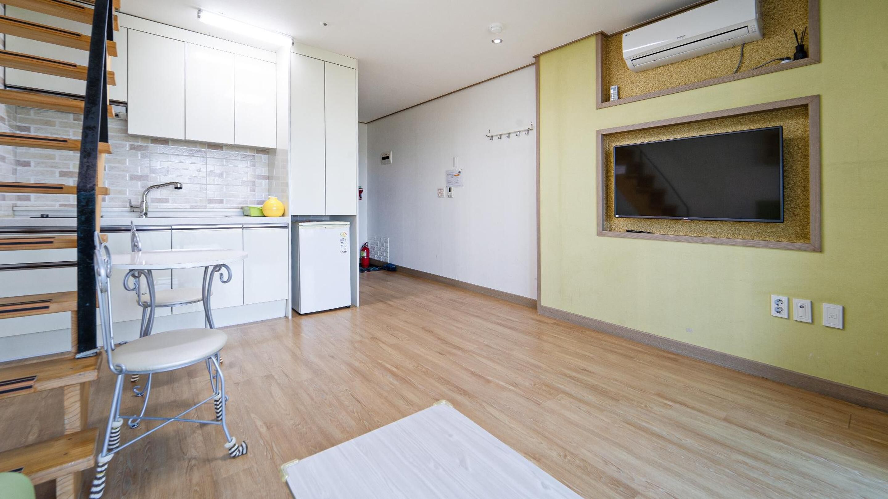 A modern kitchen with white cabinets, a small fridge, and a dining area with a metal chair.