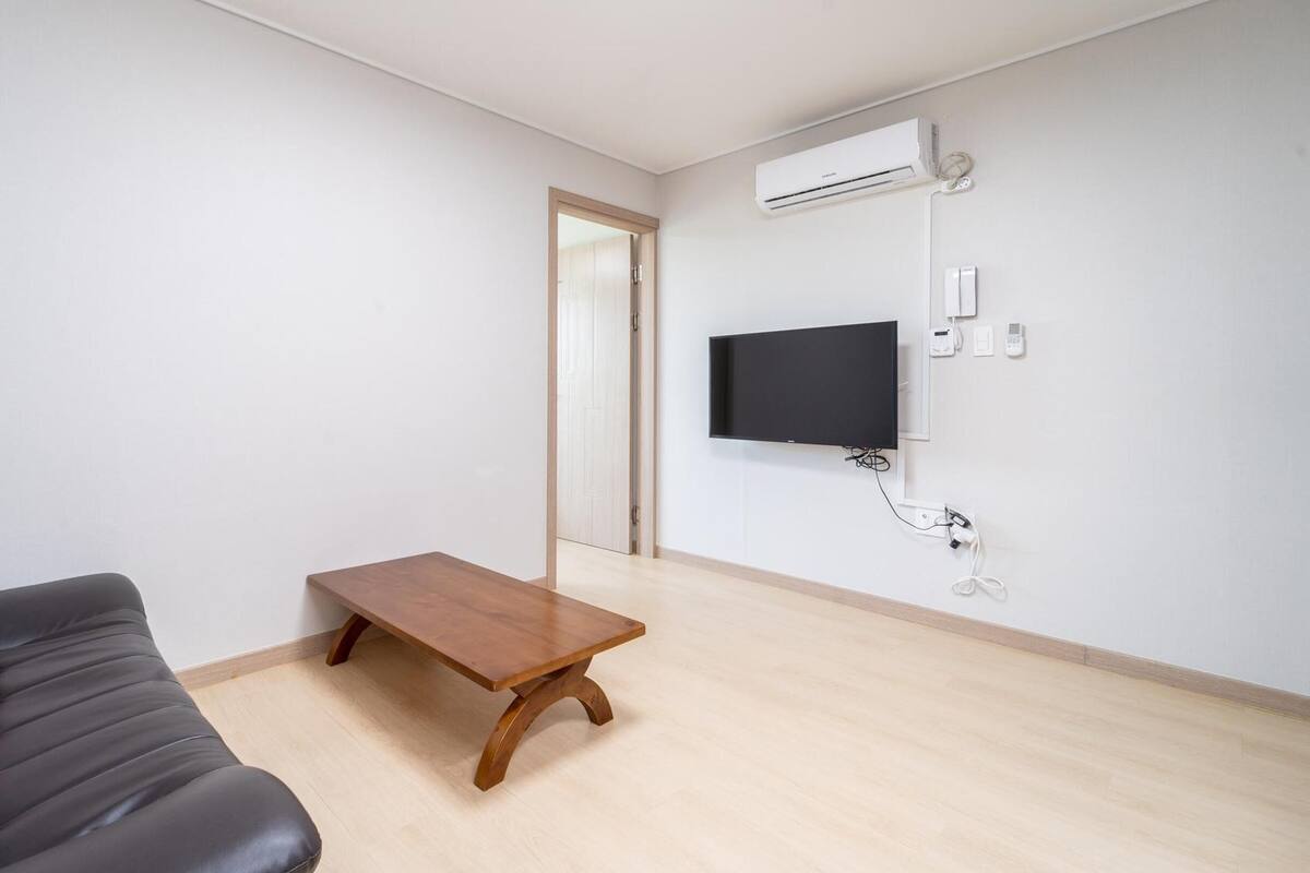 Una sala de estar moderna con un sofá de cuero, una mesa de centro de madera, un televisor de pantalla plana montado en la pared y un equipo de aire acondicionado.