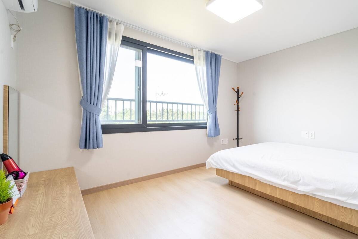 Un dormitorio con cama, cortinas en la ventana, un perchero y una planta en maceta.