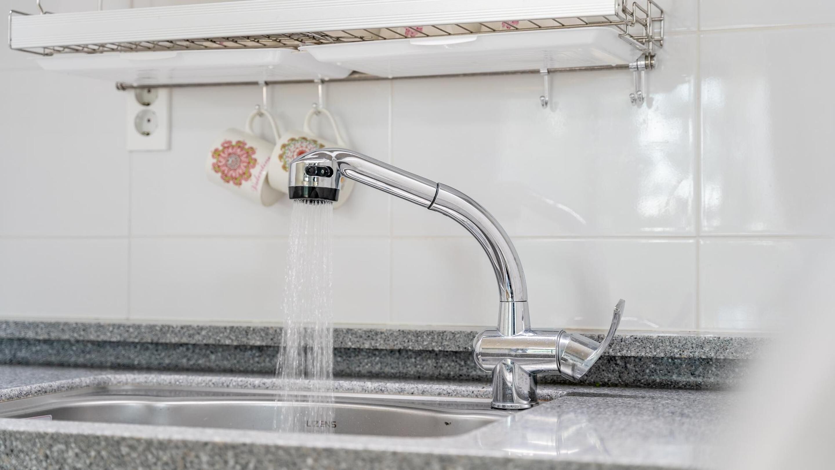 Uma pia de cozinha moderna com uma torneira cromada, bancada de granito e painel de azulejos branco.
