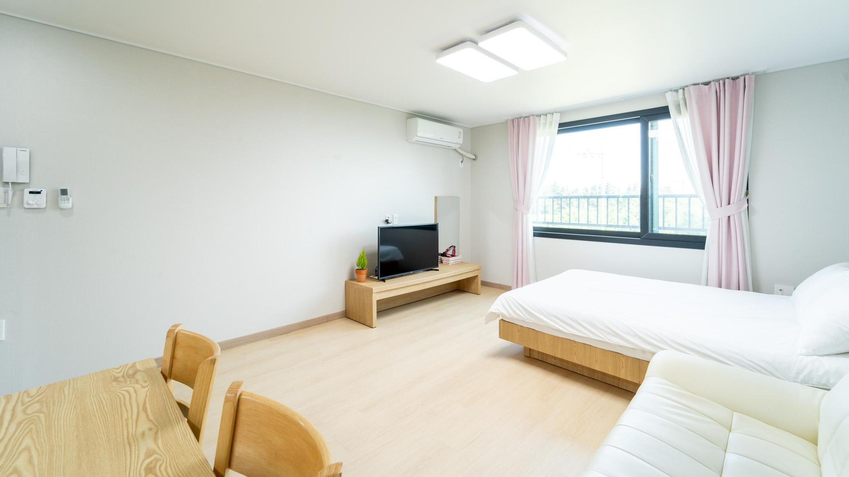 Ein Hotelzimmer mit einem Bett, einem Fernseher auf einem Holzboden, einem kleinen Tisch und einem Fenster mit Vorhängen.