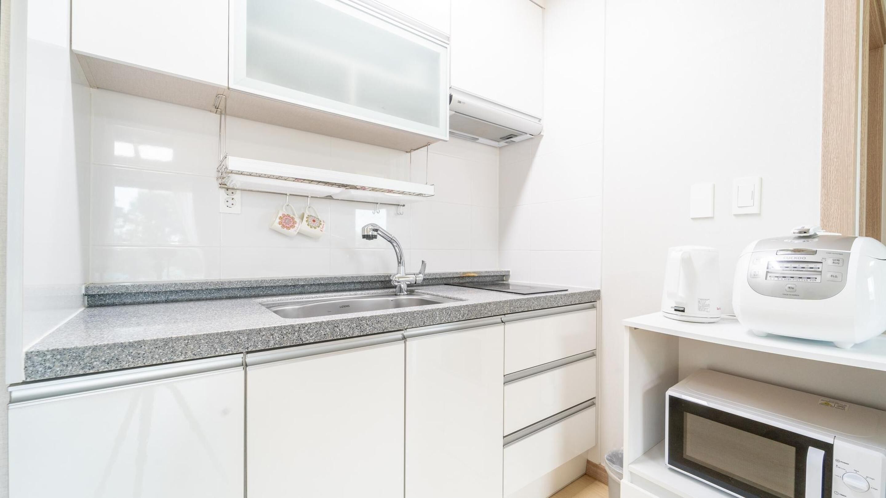 A modern kitchen with a granite countertop, stainless steel sink, white cabinets, and a built-in microwave.