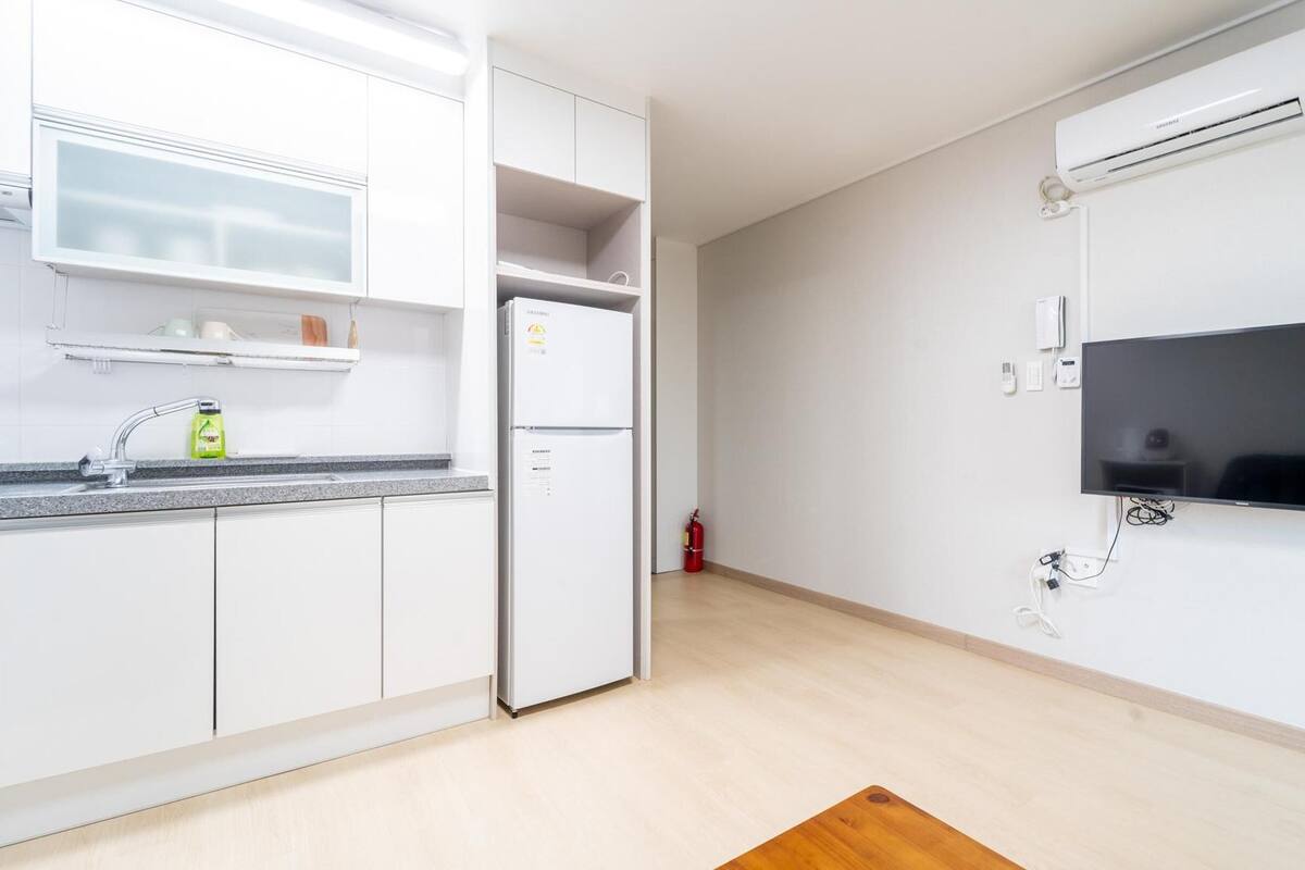 Una cocina moderna con armarios blancos, horno integrado y televisor de pantalla plana montado en la pared.