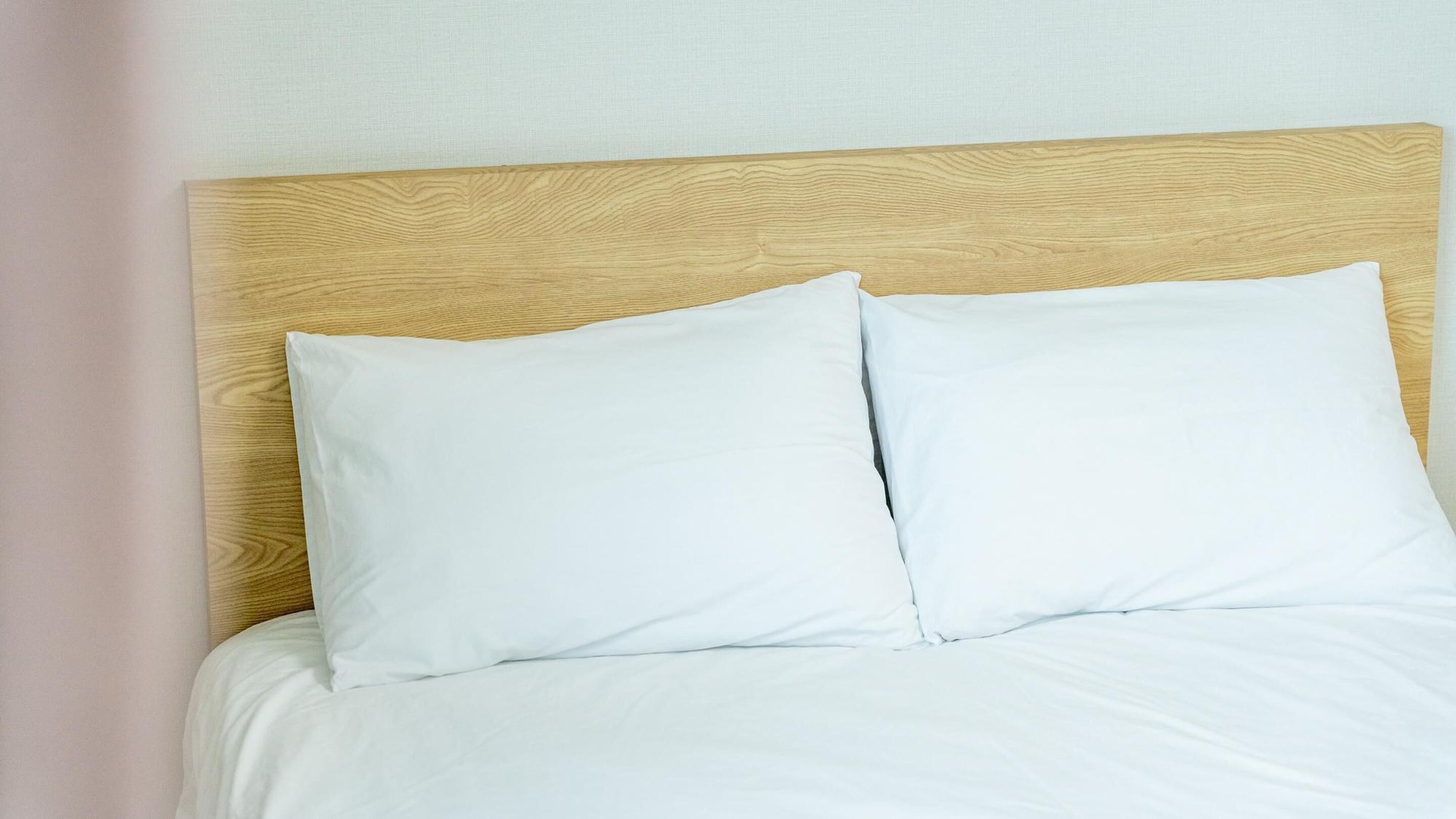 Un lit avec une tête de lit en bois et du linge de lit blanc.