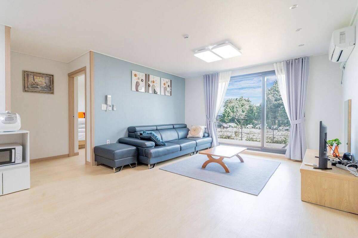 Una sala de estar moderna con un sofá gris, una cafetera, un microondas y un ventanal con cortinas.