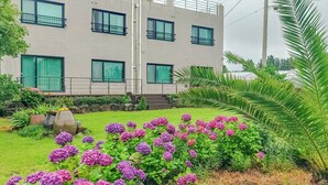 A building with multiple windows and a well-maintained garden with purple flowers.