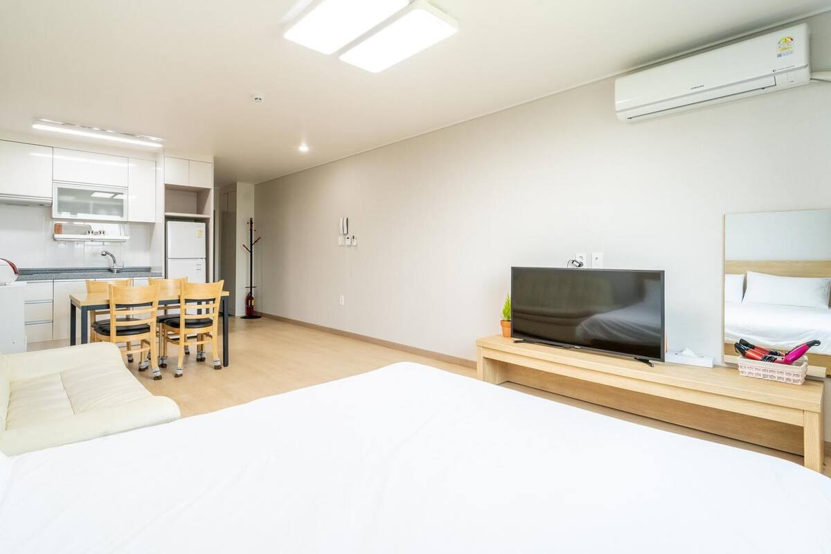 Habitación de hotel moderna con cama, televisión, pequeña cocina y mesa de comedor.