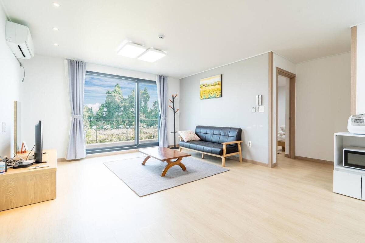 Una sala moderna con un sofá, una mesa de centro y vistas de un jardín a través de amplios ventanales.