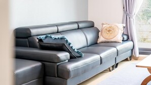 A modern living room with a dark leather sofa, decorative pillows, and a view of greenery through a window.