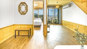 Una habitació àmplia amb terres de fusta, un llit, una banca i vista a un espai exterior amb taula i cadires a través d'una porta de vidre.