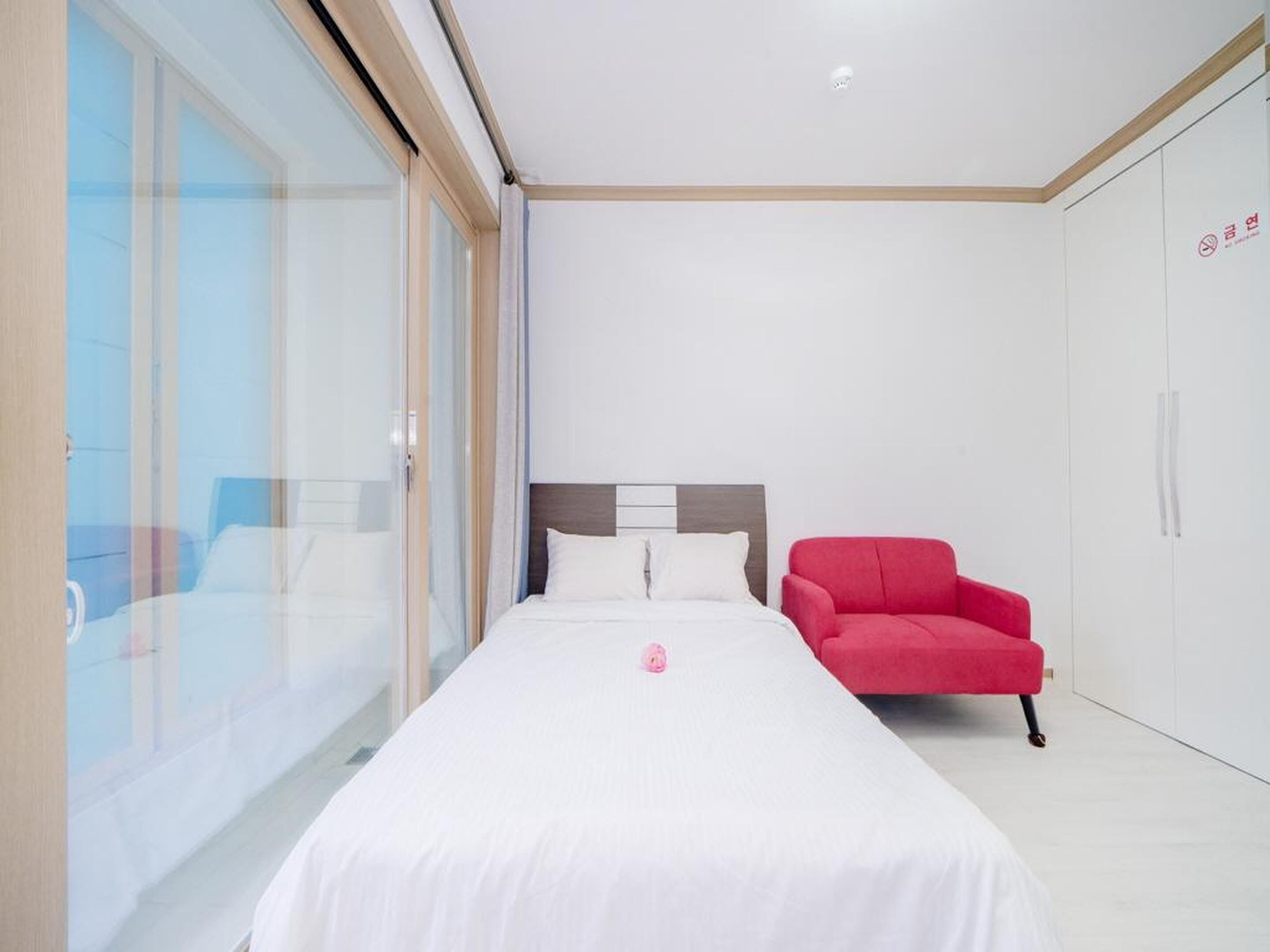 A modern hotel room with a large bed, a red armchair, and a wardrobe.