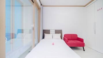A modern hotel room with a large bed, a red armchair, and a wardrobe.