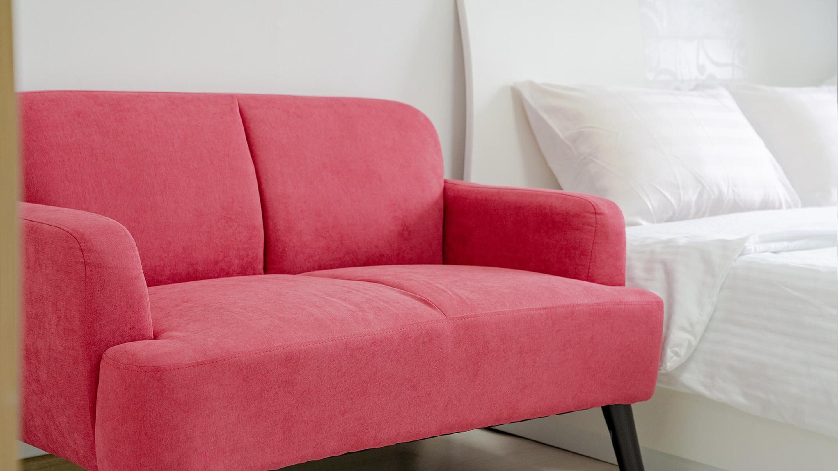 A red armchair in a bedroom with white bedding and a white headboard.