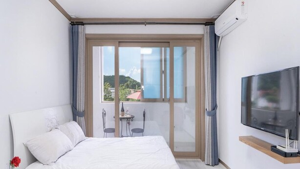 A hotel room with a bed, a TV, a balcony with a table and chairs, and a view of the outdoors. - Samcheo Happy House Pension (Samcheok)
