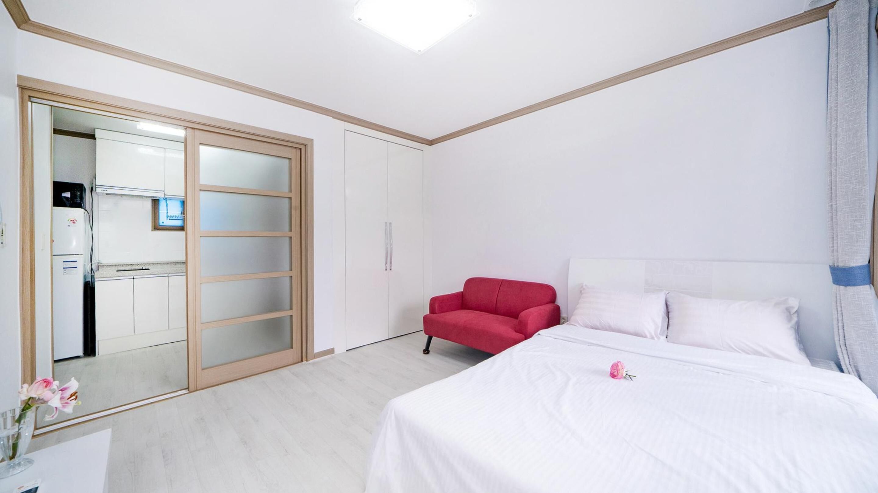 A hotel room with a bed, a red chair, a wardrobe, and a small kitchenette.