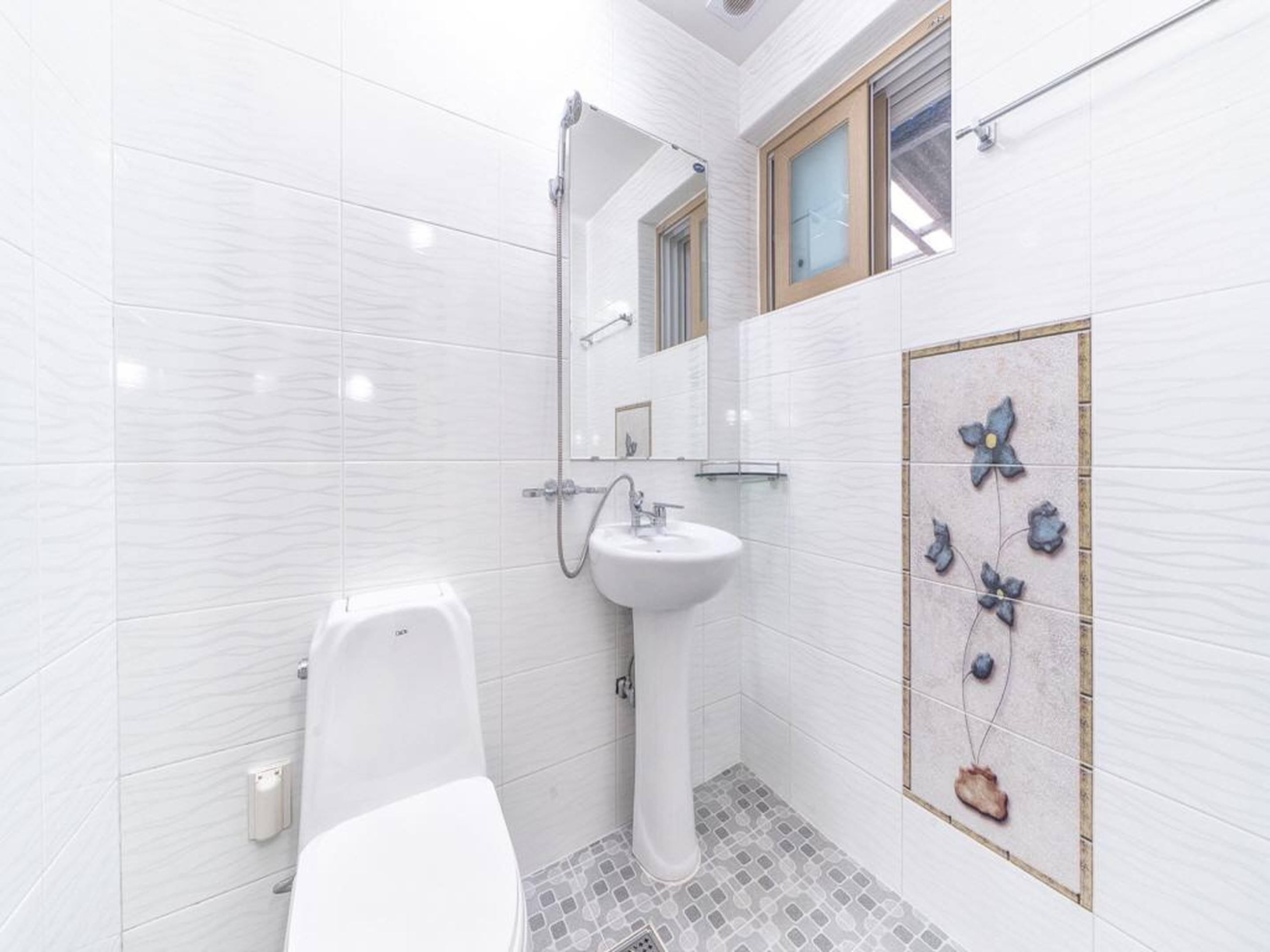 Un baño con azulejos blancos, un lavabo con pedestal, un inodoro y una ducha.