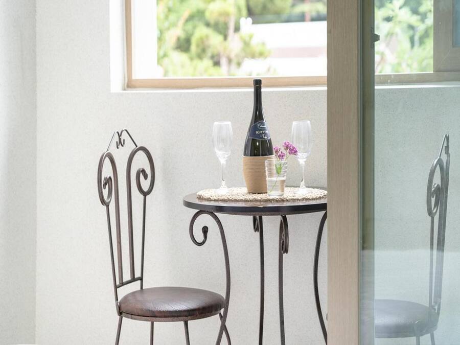 A small round table with a bottle and two glasses, a chair, and a window with a view of greenery.