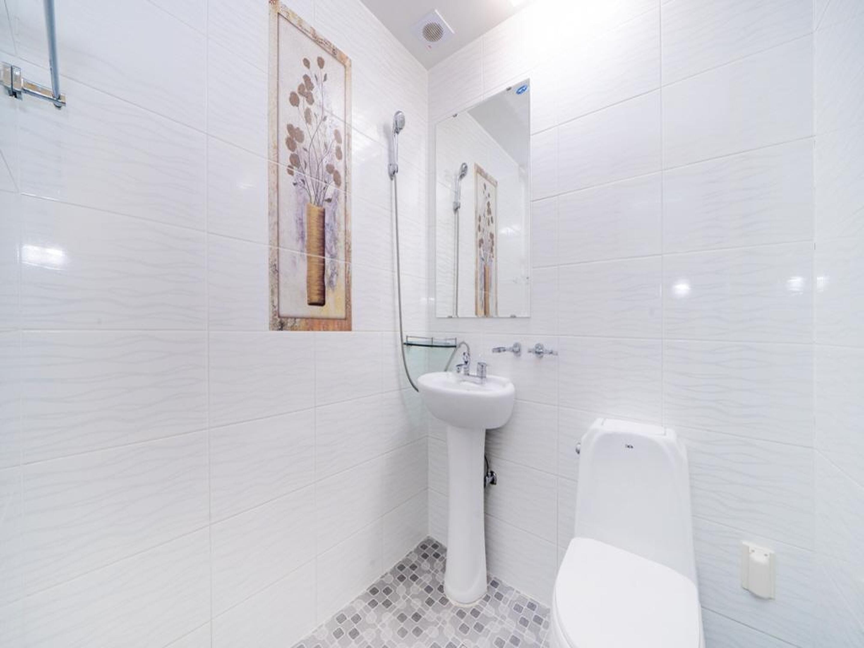 Une salle de bain moderne avec des carreaux blancs, une douche en verre, un lavabo sur colonne et des toilettes.