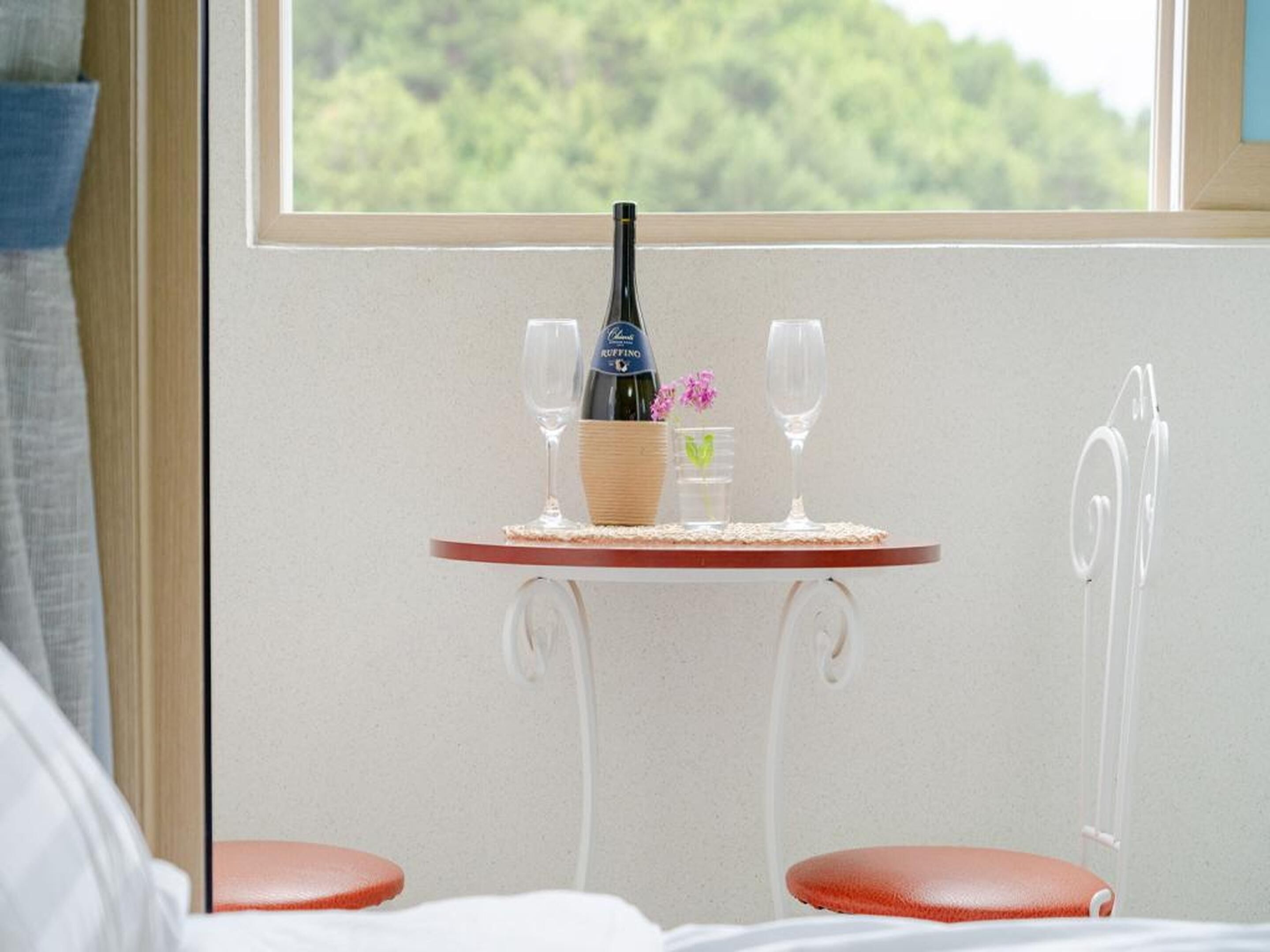 A small table with a bottle of wine, two glasses, and a small vase with flowers.